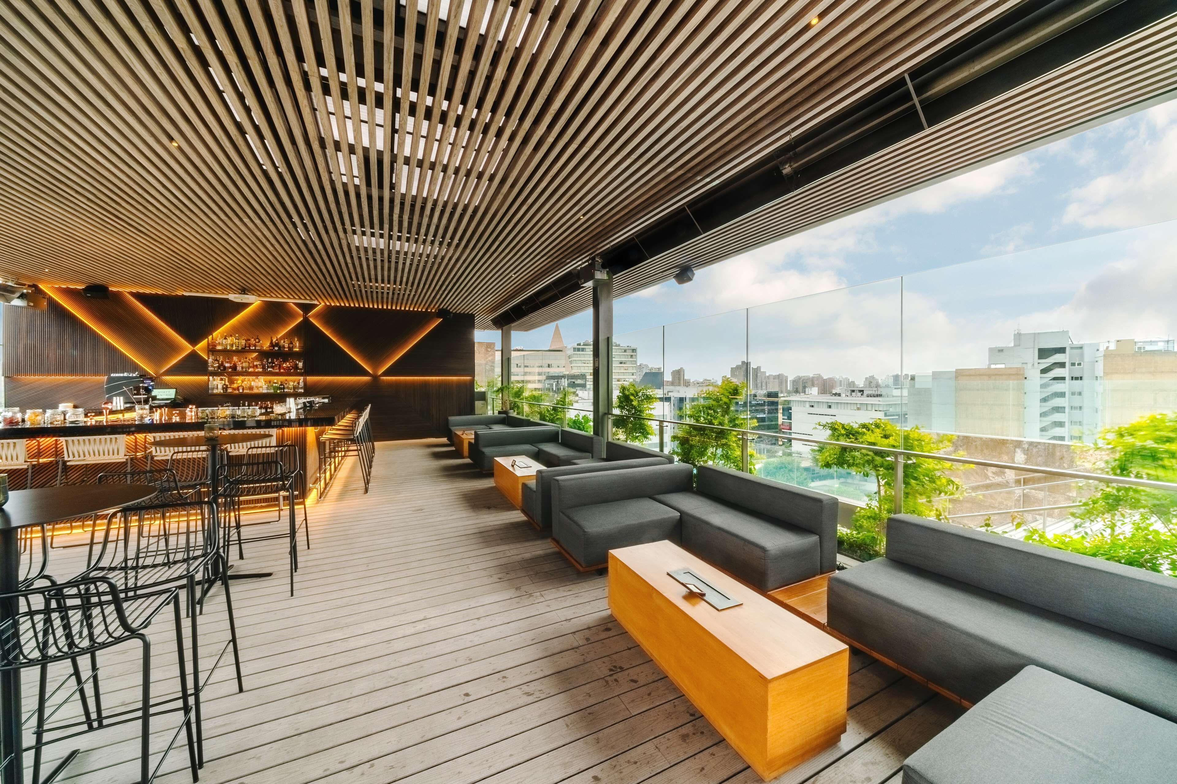 Un bar en la azotea con suelo de madera, taburetes de bar y una zona de estar con sofás y una mesa de centro.