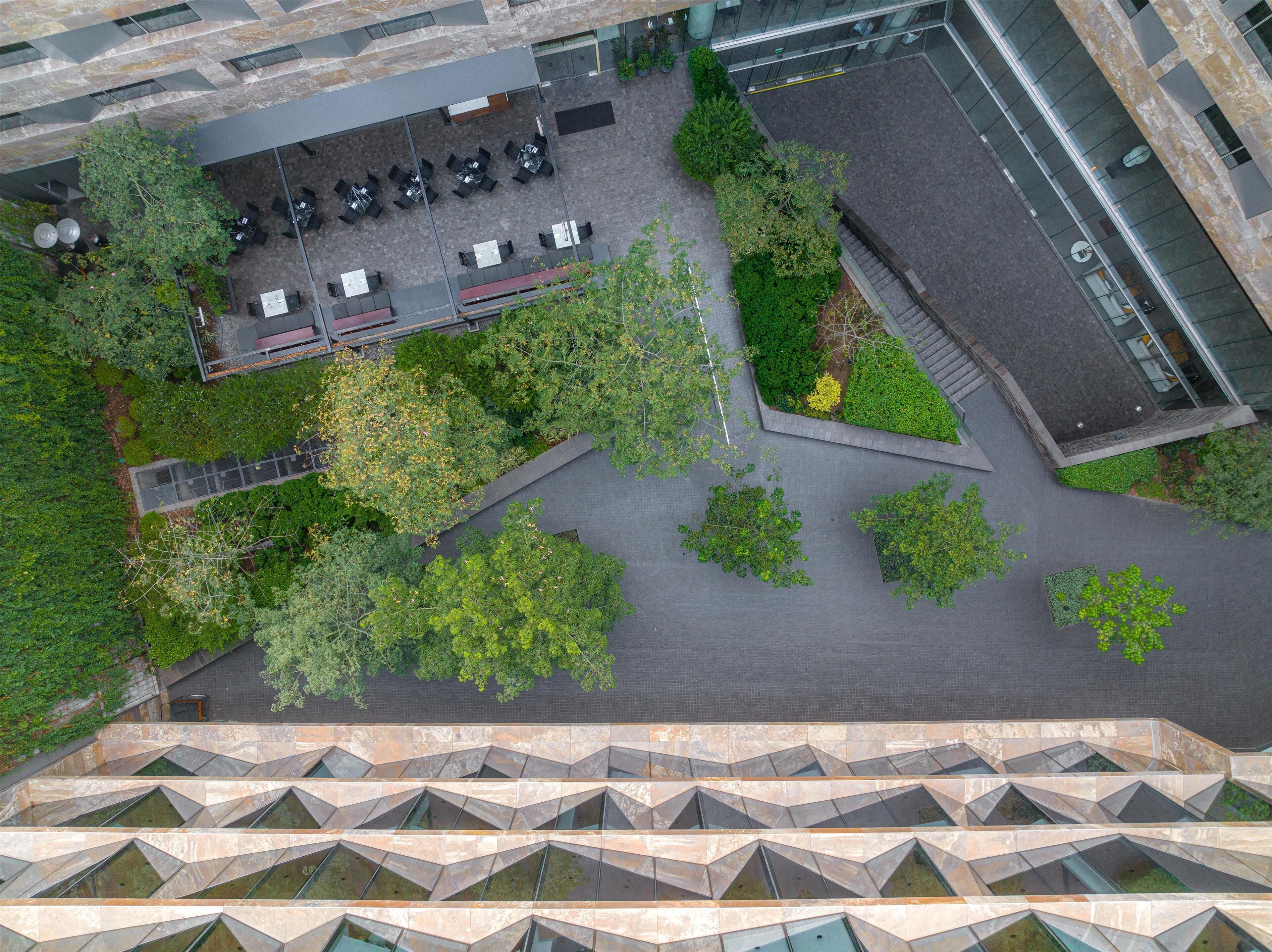 An aerial view of a modern building with a rooftop garden, outdoor seating area, and a parking lot.