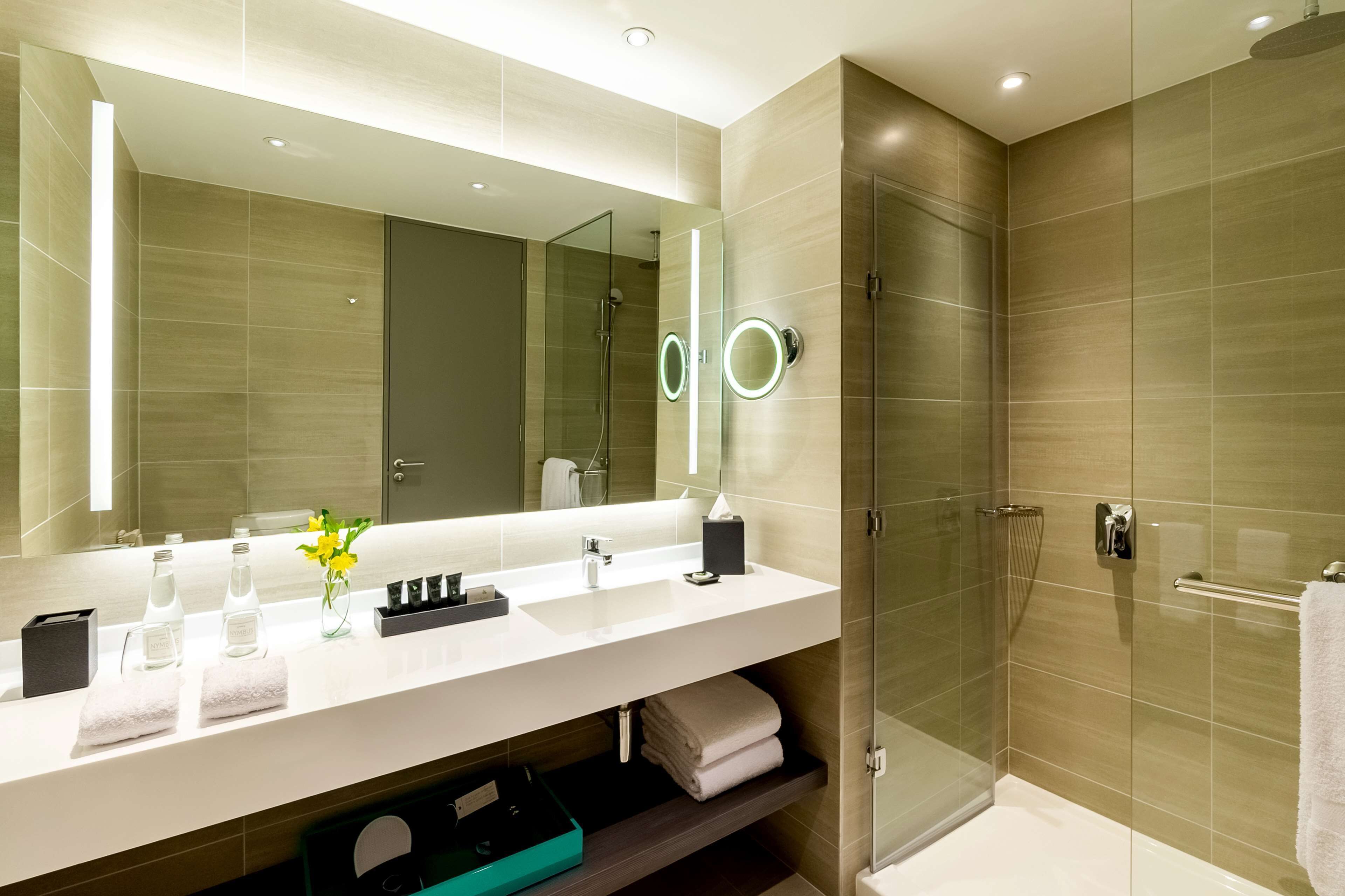 Un baño moderno con un espejo grande, cabina de ducha de vidrio y tocador con lavamanos y toallero.
