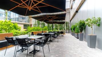 Une terrasse extérieure avec des tables et des chaises, protégée par de grands parasols et entourée de verdure.