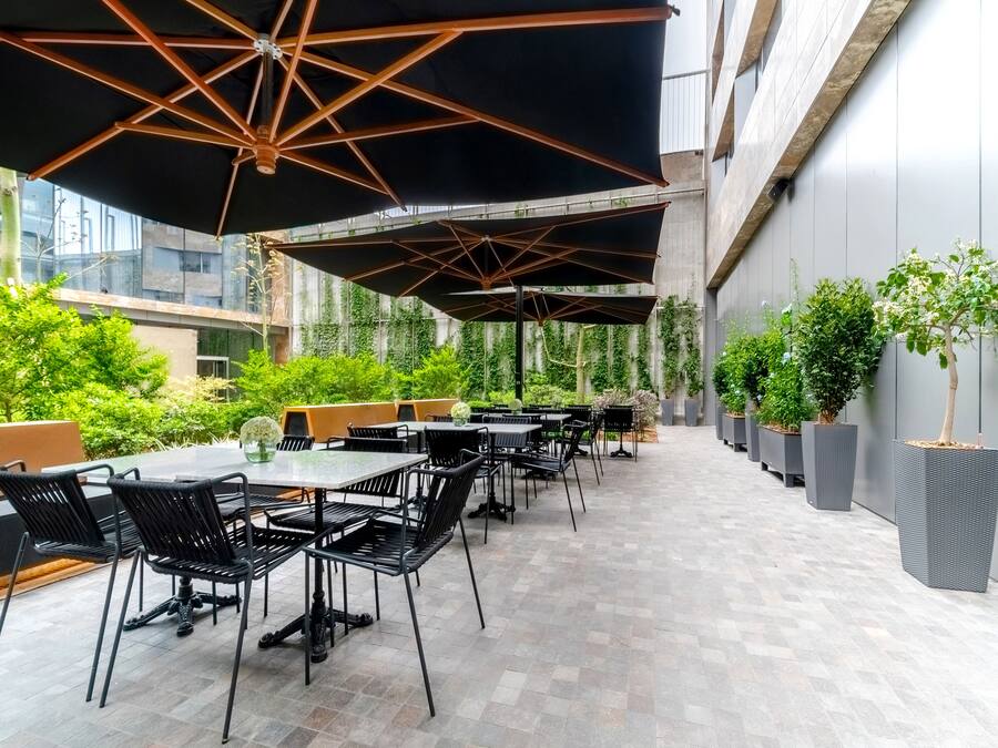 Une terrasse extérieure avec des tables et des chaises, protégée par de grands parasols et entourée de verdure.