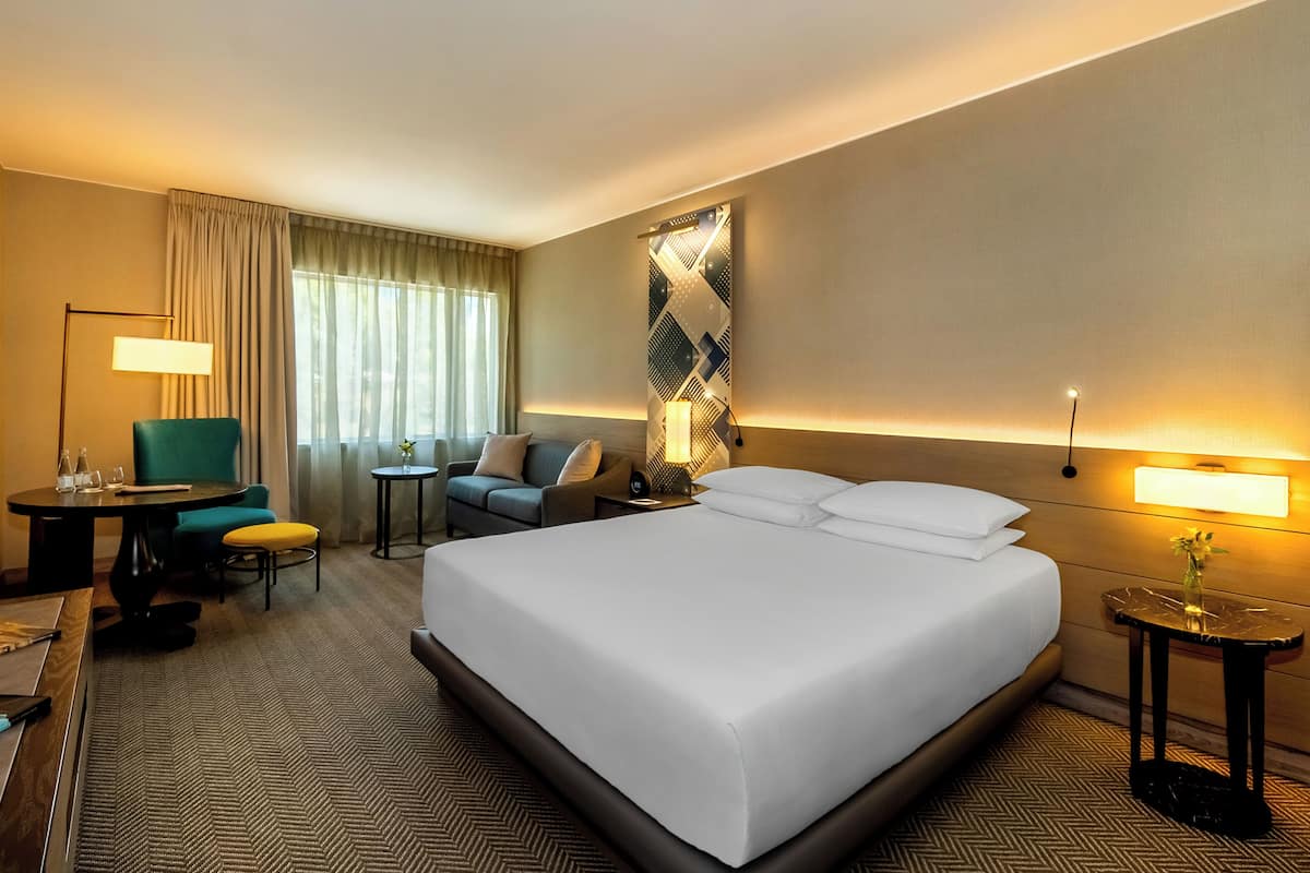 Habitación de hotel con una cama grande, un escritorio con silla, un sofá, una mesita y una lámpara.