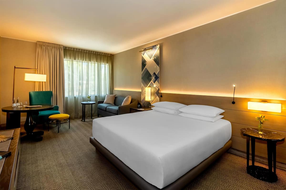 Una habitación de hotel con una cama grande, un escritorio, una silla, un sofá y una mesita de noche con lámpara.