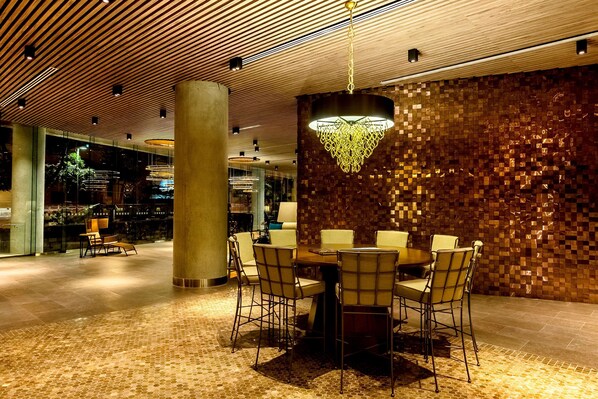 A modern dining area with a round table and chairs, a patterned wall, and a hanging chandelier.