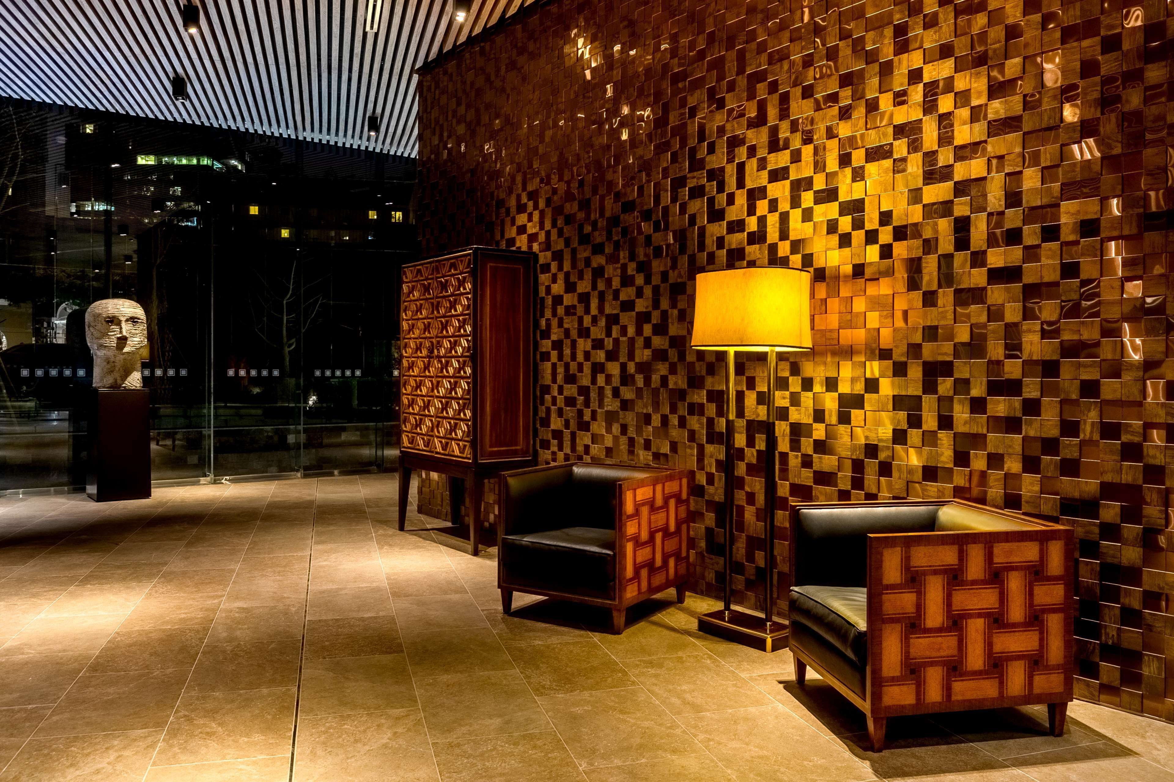 Um saguão com parede de madeira quadriculada, uma luminária moderna e uma escultura.