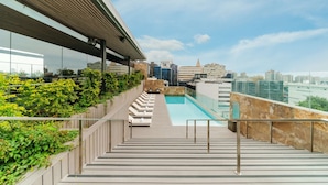 Un área de piscina en la azotea con vistas despejadas del horizonte de la ciudad, una terraza de madera y sillones de descanso.