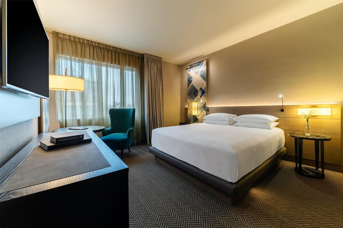 Una habitación de hotel con cama, escritorio, silla, televisor y lámpara.