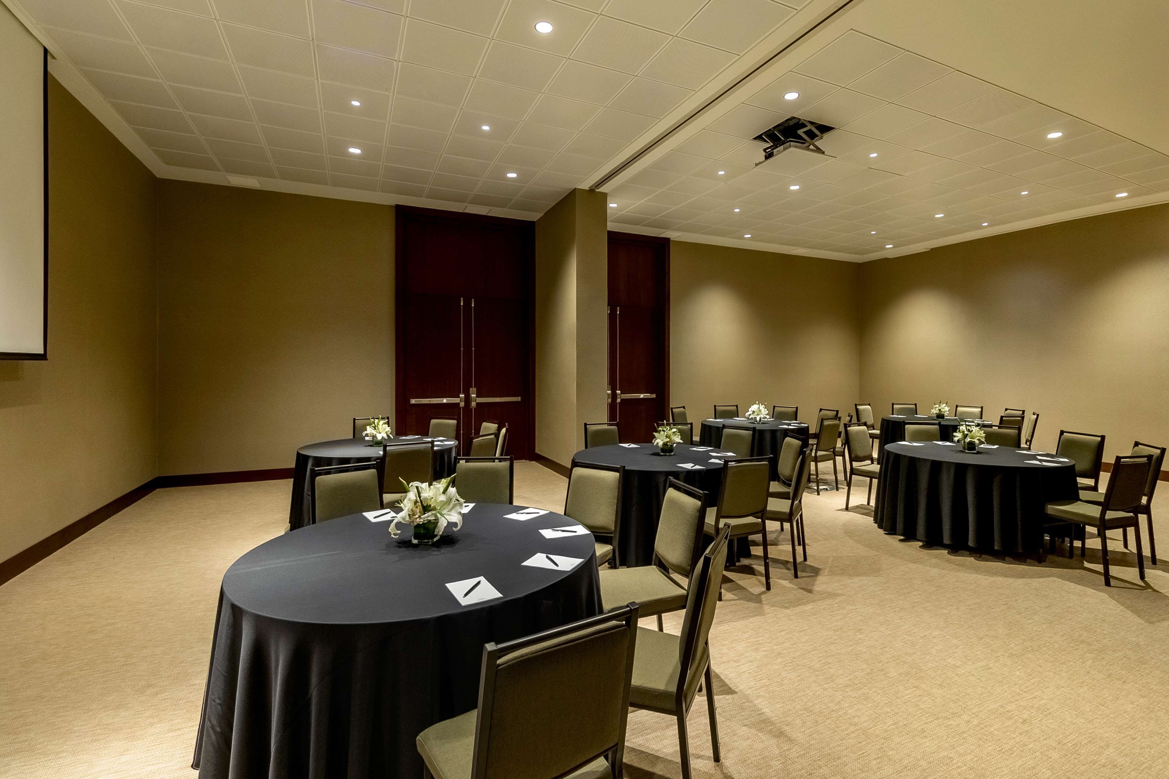 Un salón de conferencias con varias mesas redondas, sillas y una pantalla para proyector.
