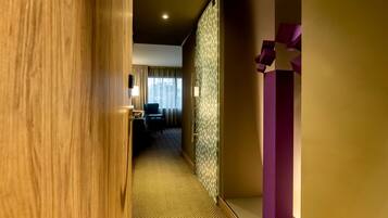 Un pasillo de hotel con una puerta de madera, papel tapiz estampado y un adorno morado.