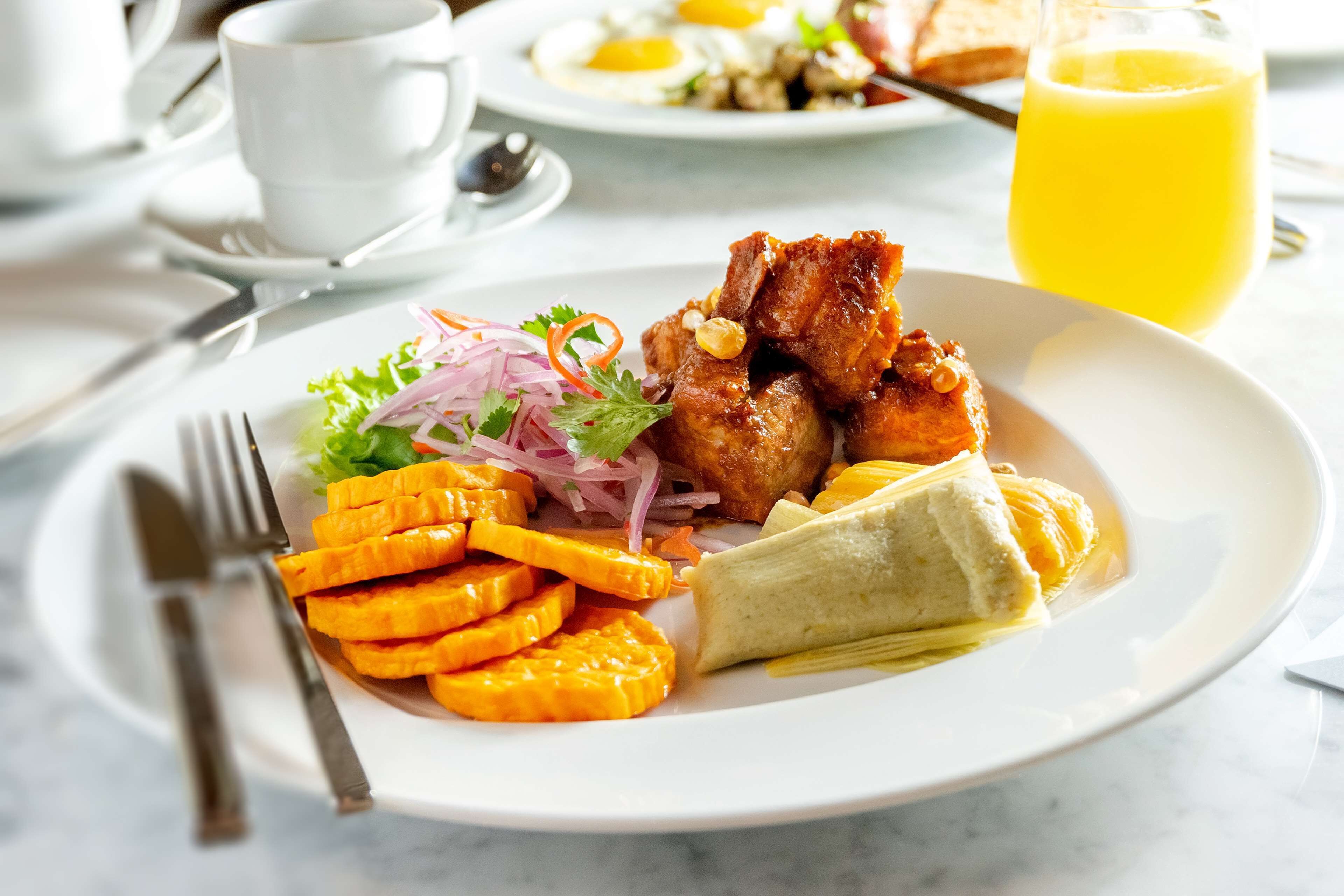 Un plato de desayuno con carne, verduras y un vaso de jugo de naranja.