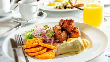 Un plato de desayuno con carne, verduras y un vaso de jugo de naranja.