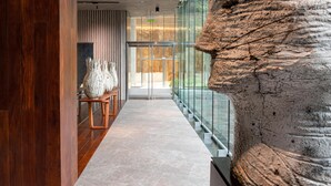 Un interior moderno con una escultura de piedra, suelo de madera y barandilla de cristal.
