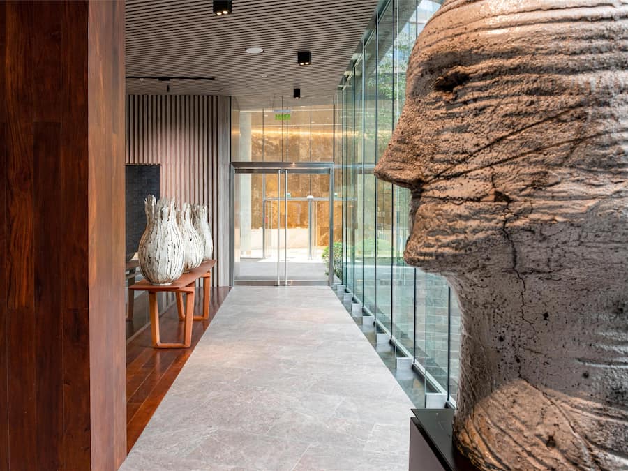 Un interior moderno con una escultura de piedra, suelo de madera y barandilla de cristal.