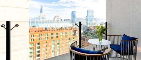 A balcony with a city view, a round table, two chairs, and a vase with flowers.