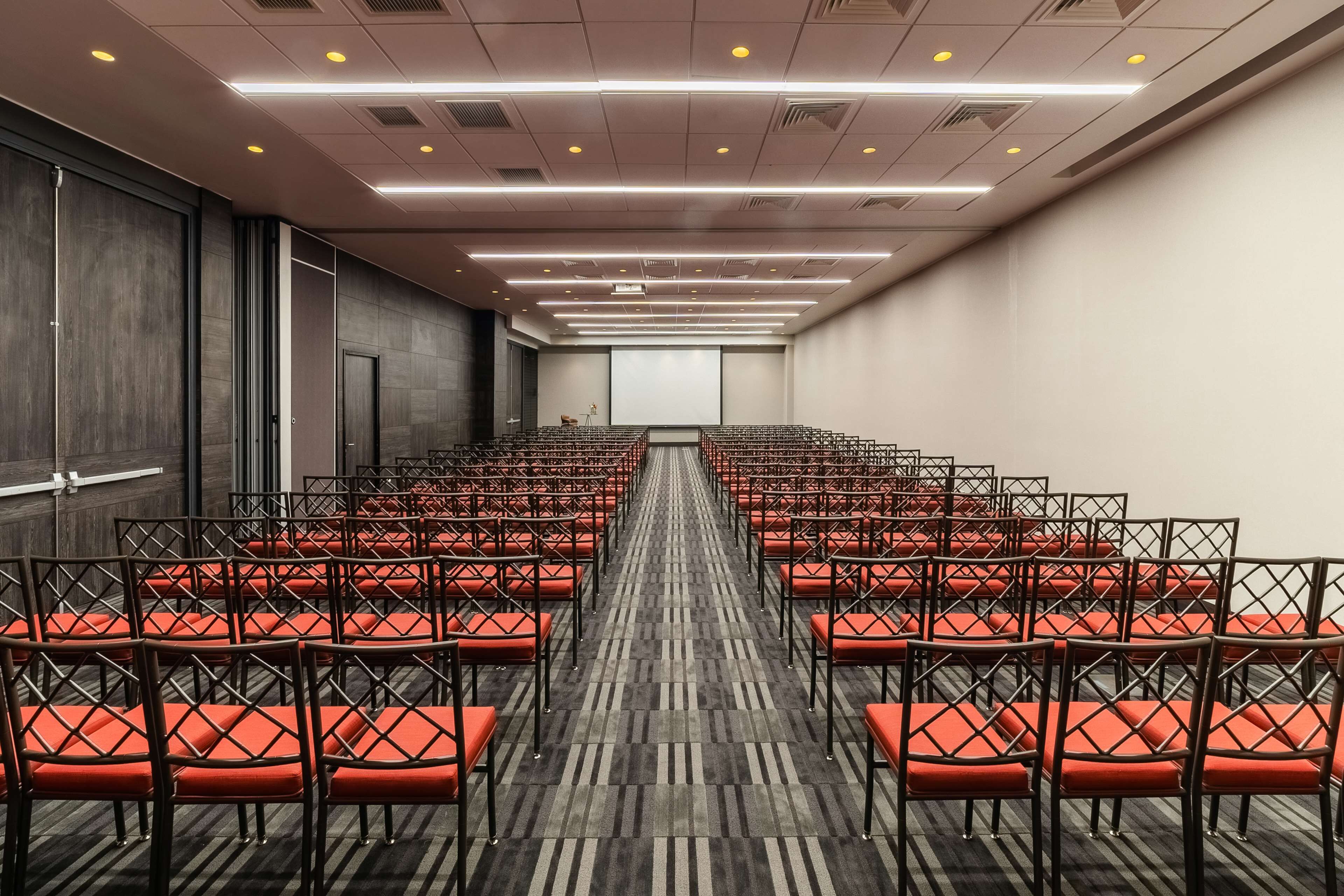 A conference room with rows of red chairs, a carpeted floor, and a projector screen at the front.