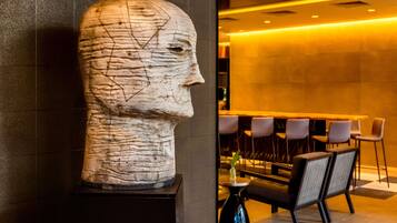 A sculpture of a human head on a pedestal in a modern lobby with a bar and seating area.