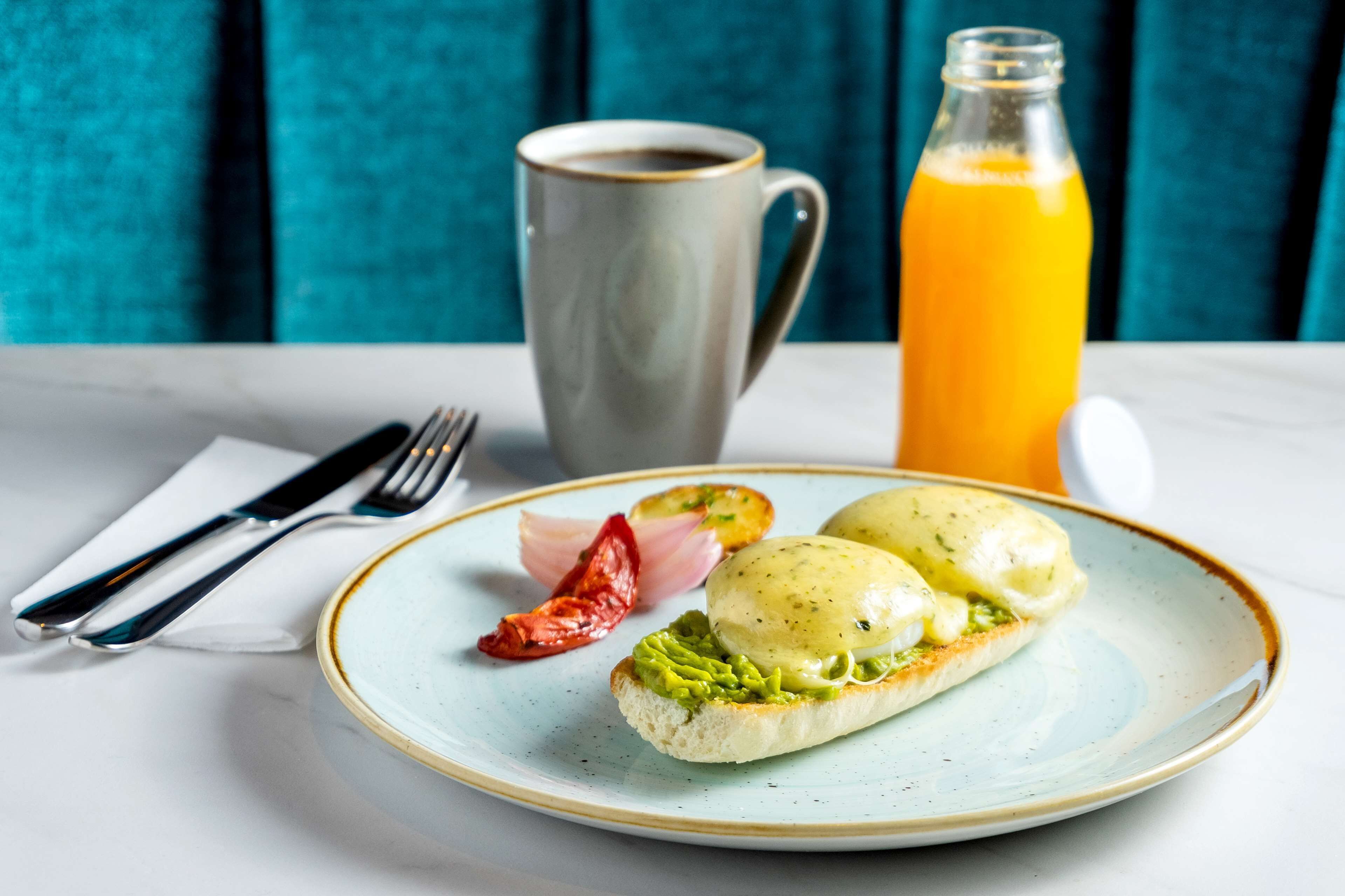 A plate with eggs benedict, a glass of orange juice, and a cup of coffee on a table.