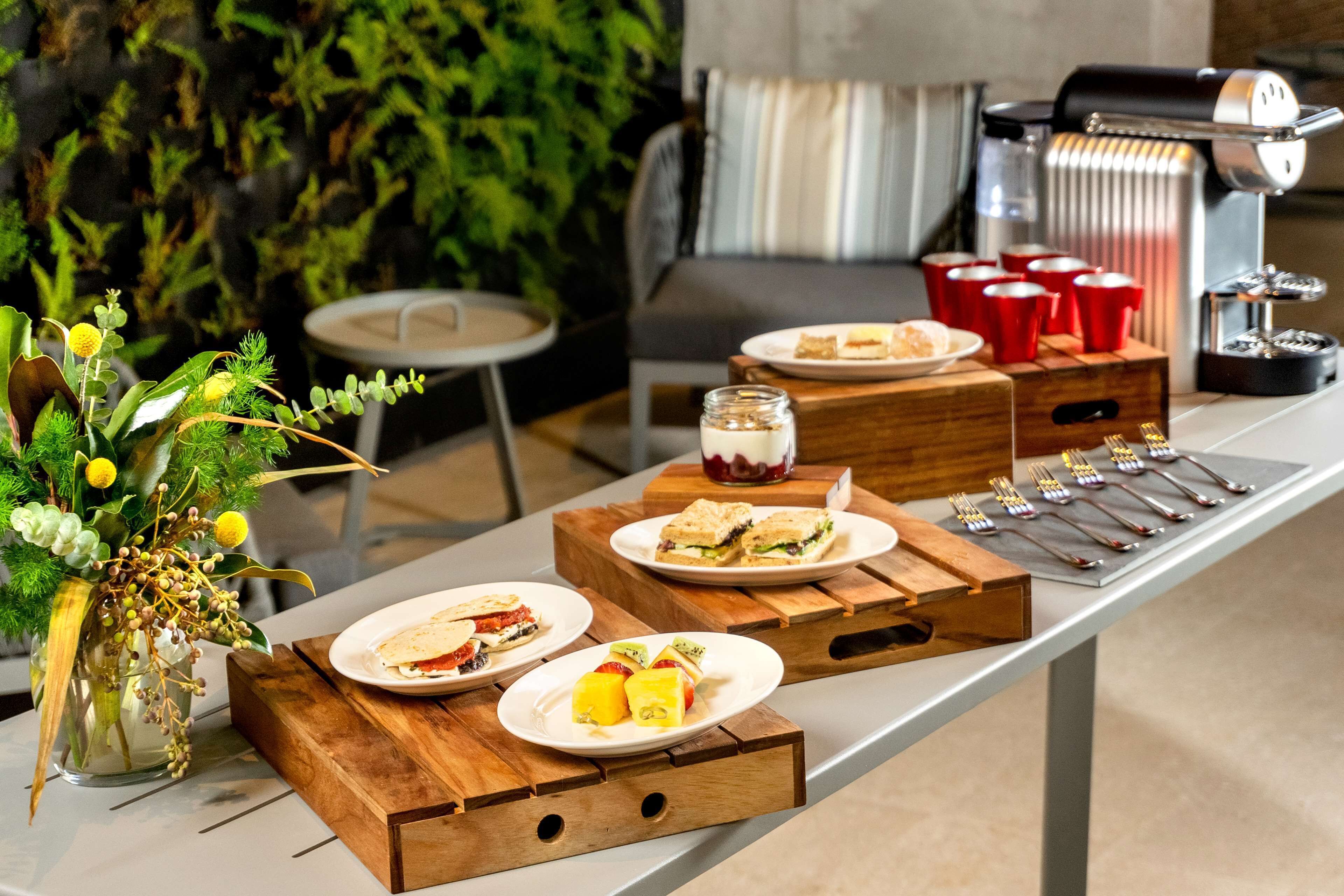A breakfast buffet setup with various food items, a coffee machine, and a decorative plant.