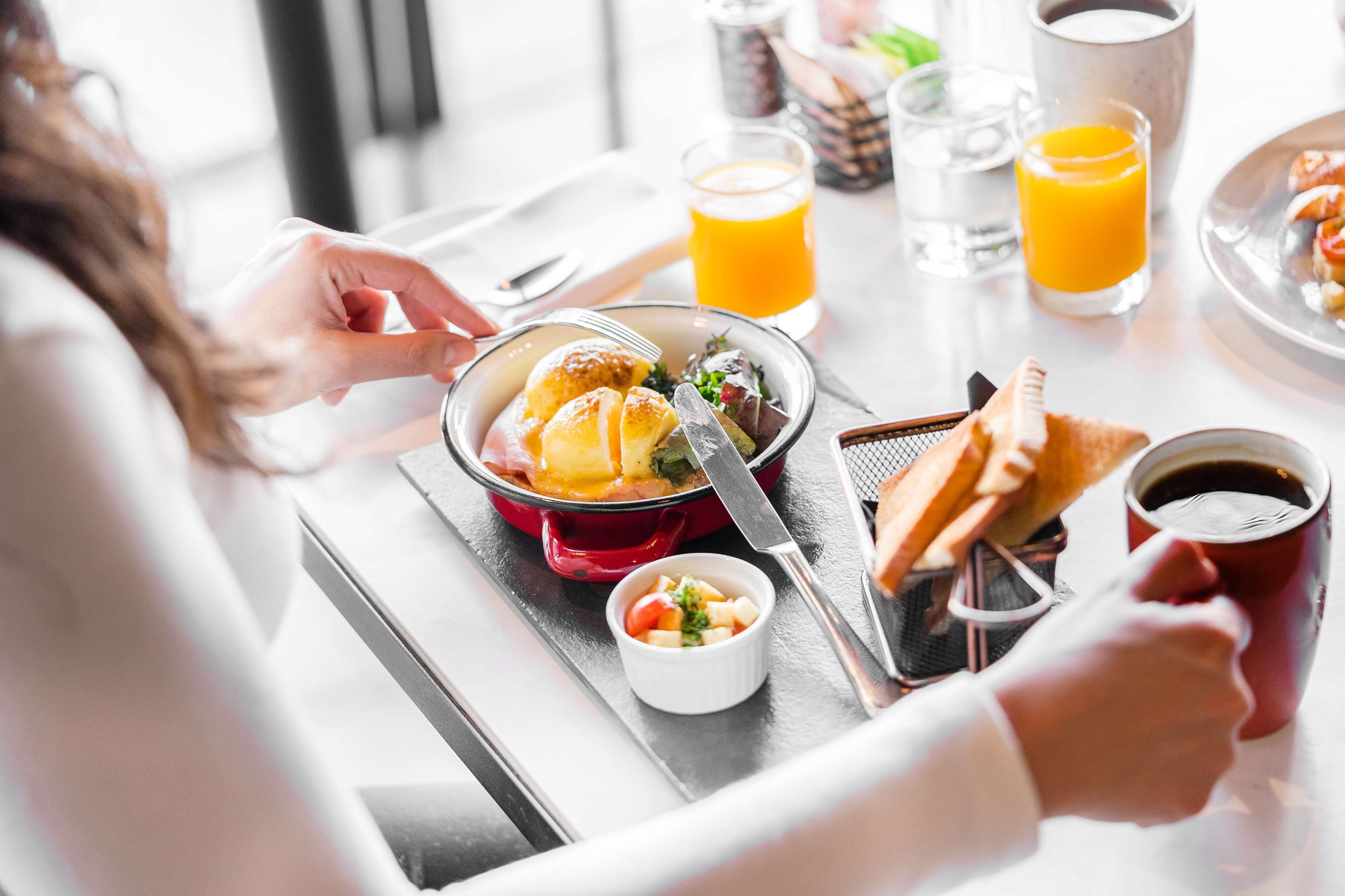 A breakfast setting with a red pot, a small bowl of fruit, a cup of coffee, and a glass of orange juice on a tray.