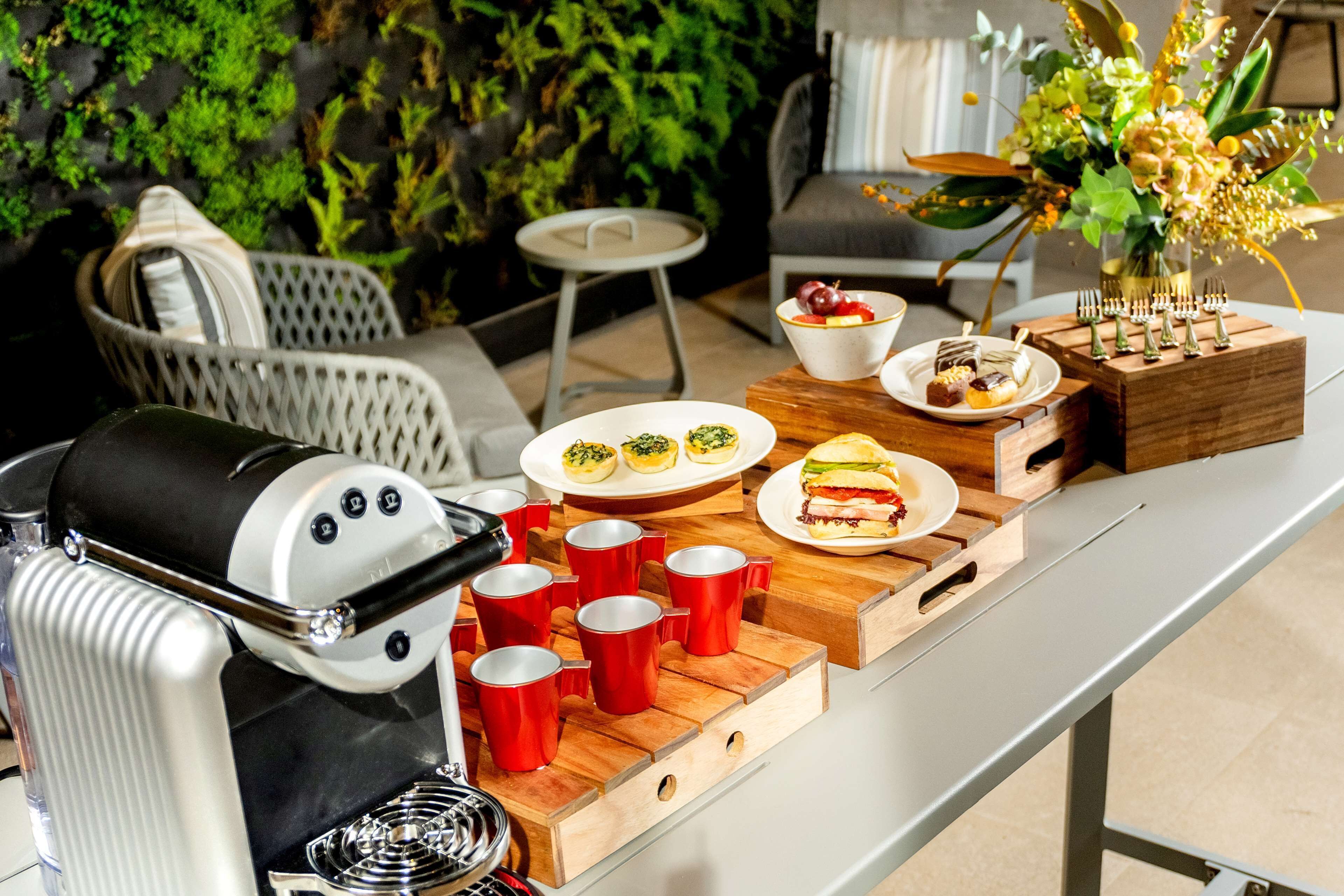 A dining area with a coffee machine, red cups, plates with food, and a decorative vase.