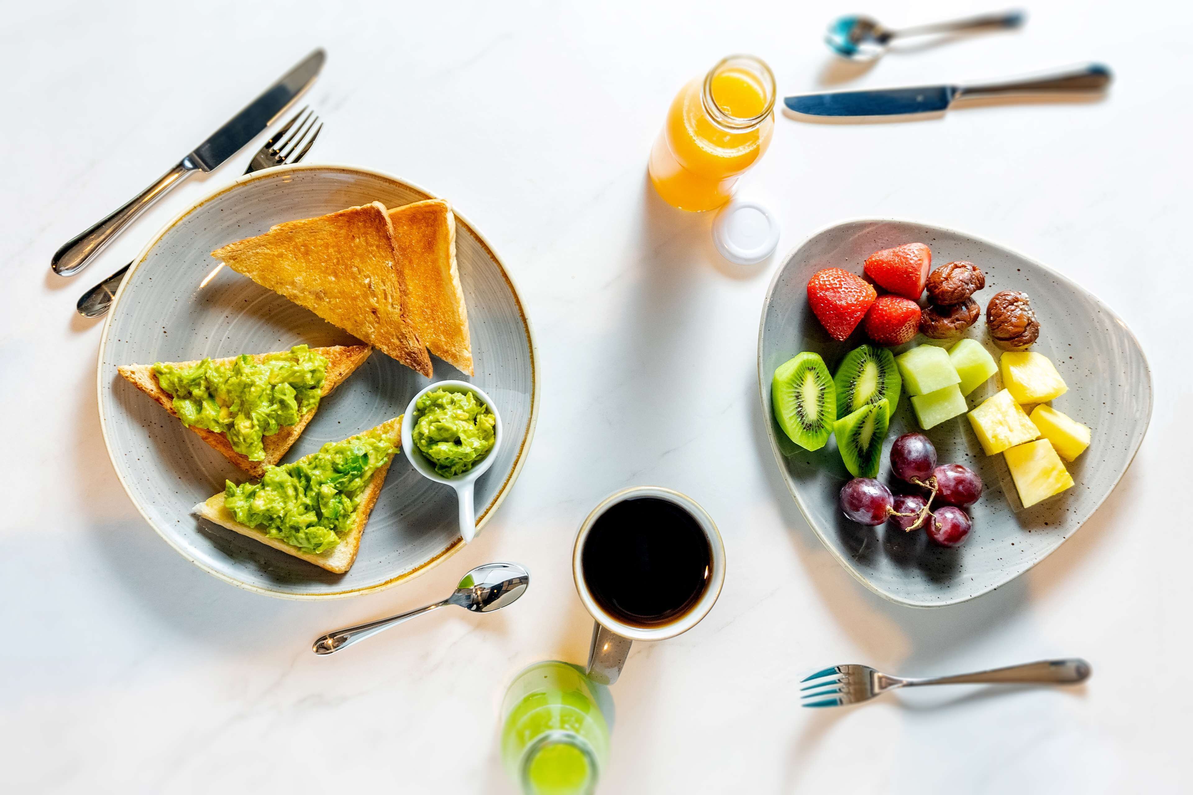 Uma mesa de café da manhã com torradas, abacate, uma xícara de café e um prato de frutas.