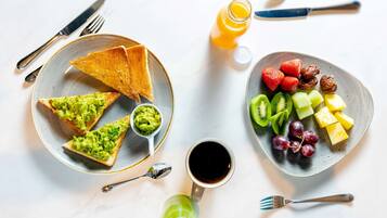Uma mesa de café da manhã com torradas, abacate, uma xícara de café e um prato de frutas.