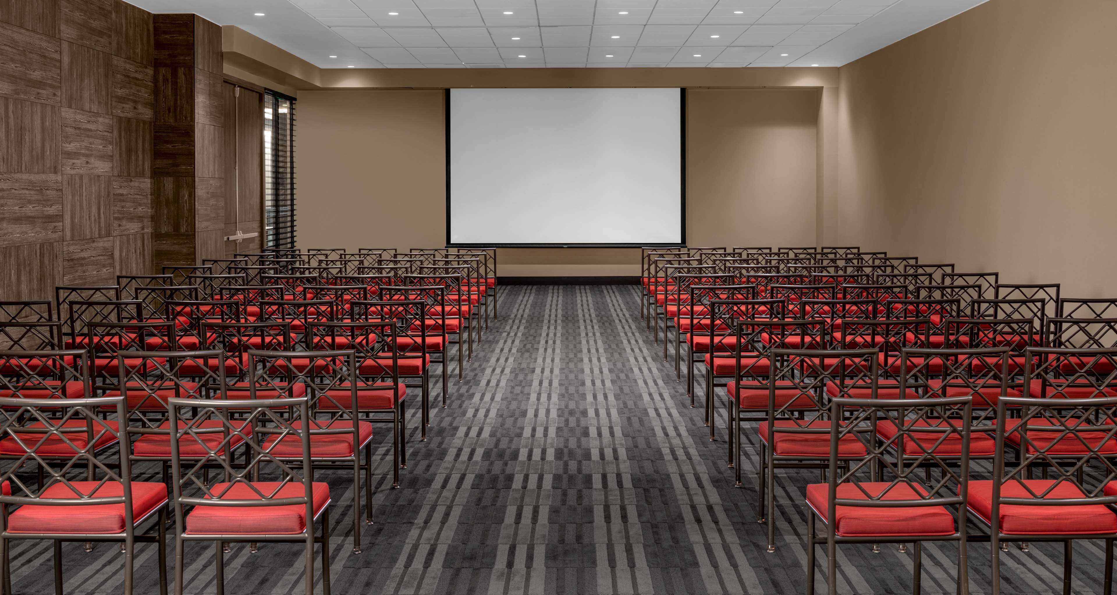 Un salón de conferencias con hileras de sillas rojas y una pantalla de proyección grande.