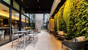 Un patio interior con mesa y sillas, un sofá, y una pared cubierta de follaje verde.
