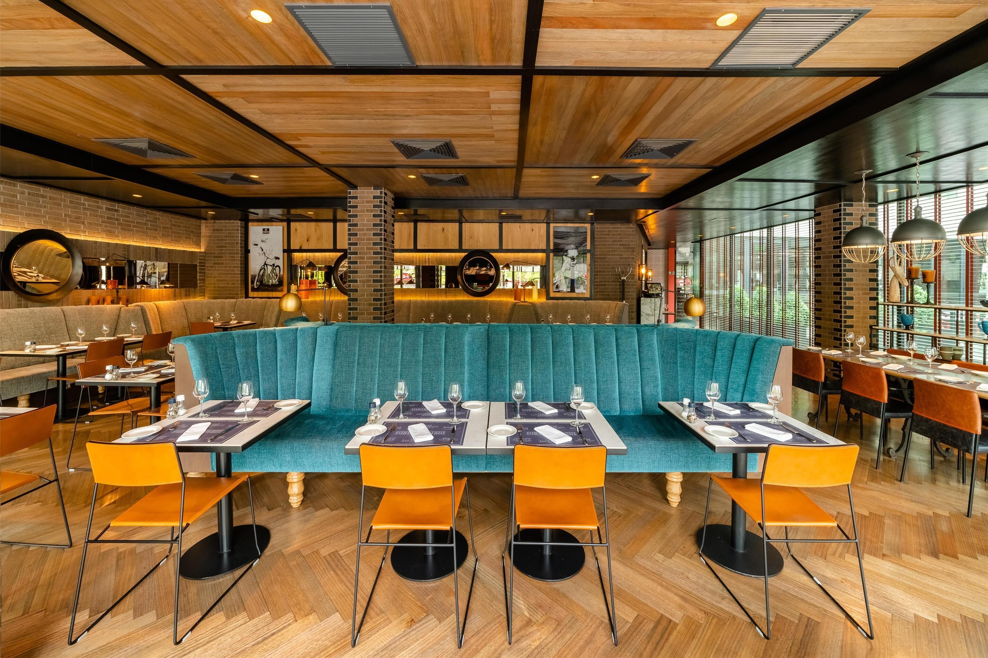 A restaurant with a teal booth seating area, wooden ceiling, and modern decor.