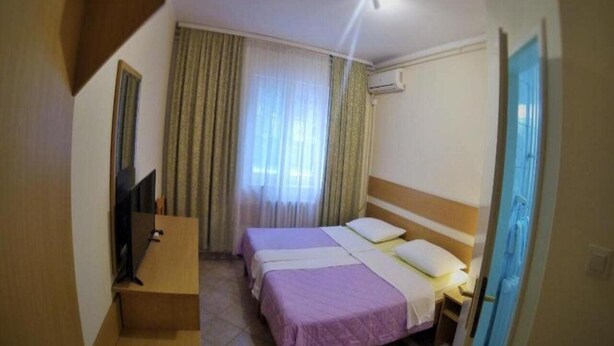 A hotel room with two beds, a desk, a TV, and a window with curtains.
