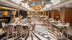 A modern dining area with multiple tables and chairs, a central chandelier, and a high ceiling with skylights. - Niepce Paris Hotel, Curio Collection by Hilton (Paris)