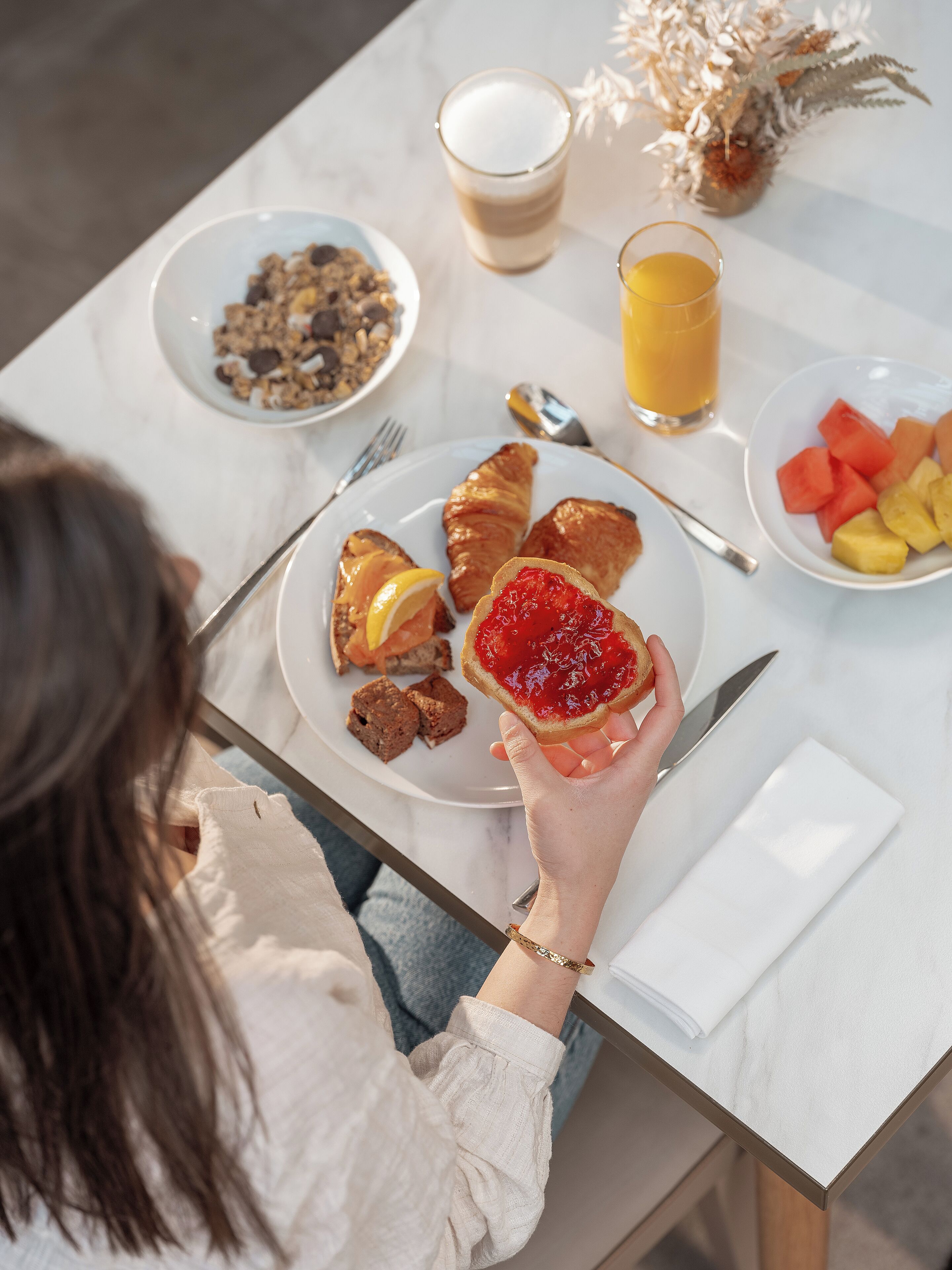Ein Frühstückstisch mit Croissants, Obst, Orangensaft und einer Schüssel Müsli.