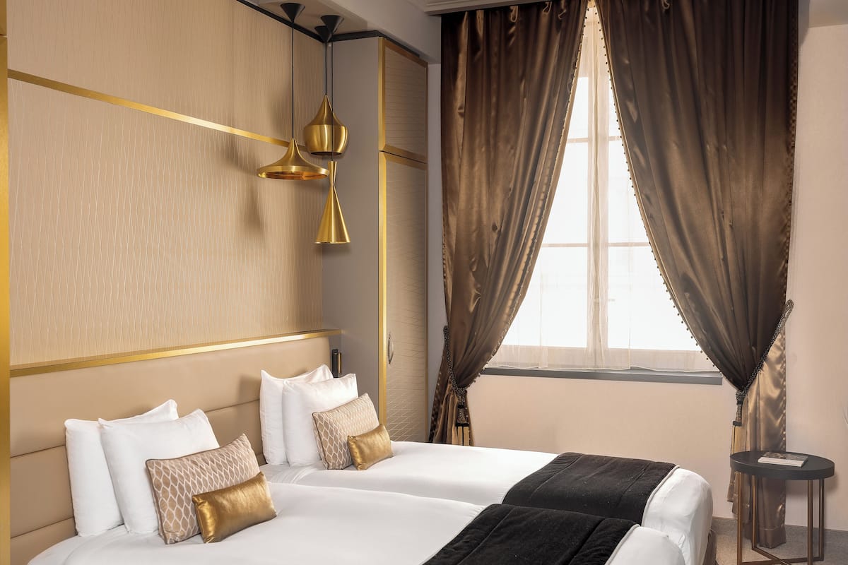 A hotel room with two beds, a small side table, and a window with curtains.