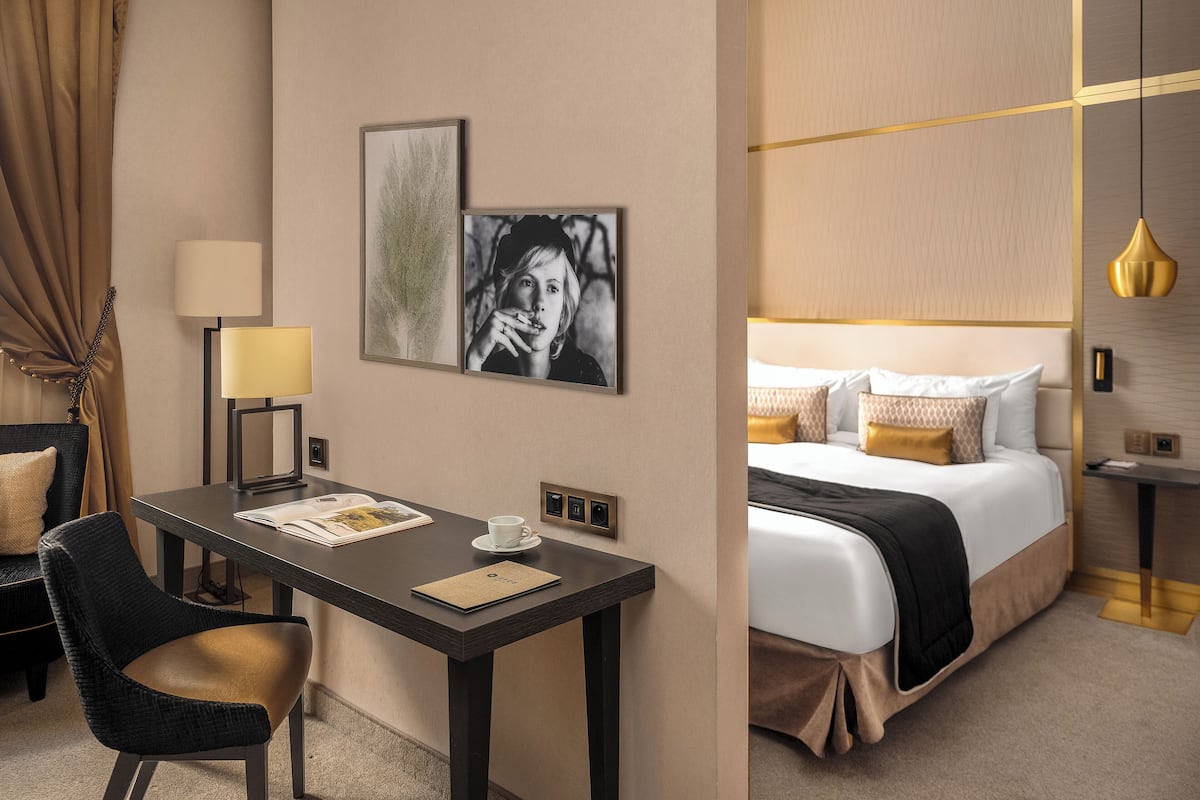 A hotel room with a bed, bedside tables, a desk with a chair, a lamp, and artwork on the wall.