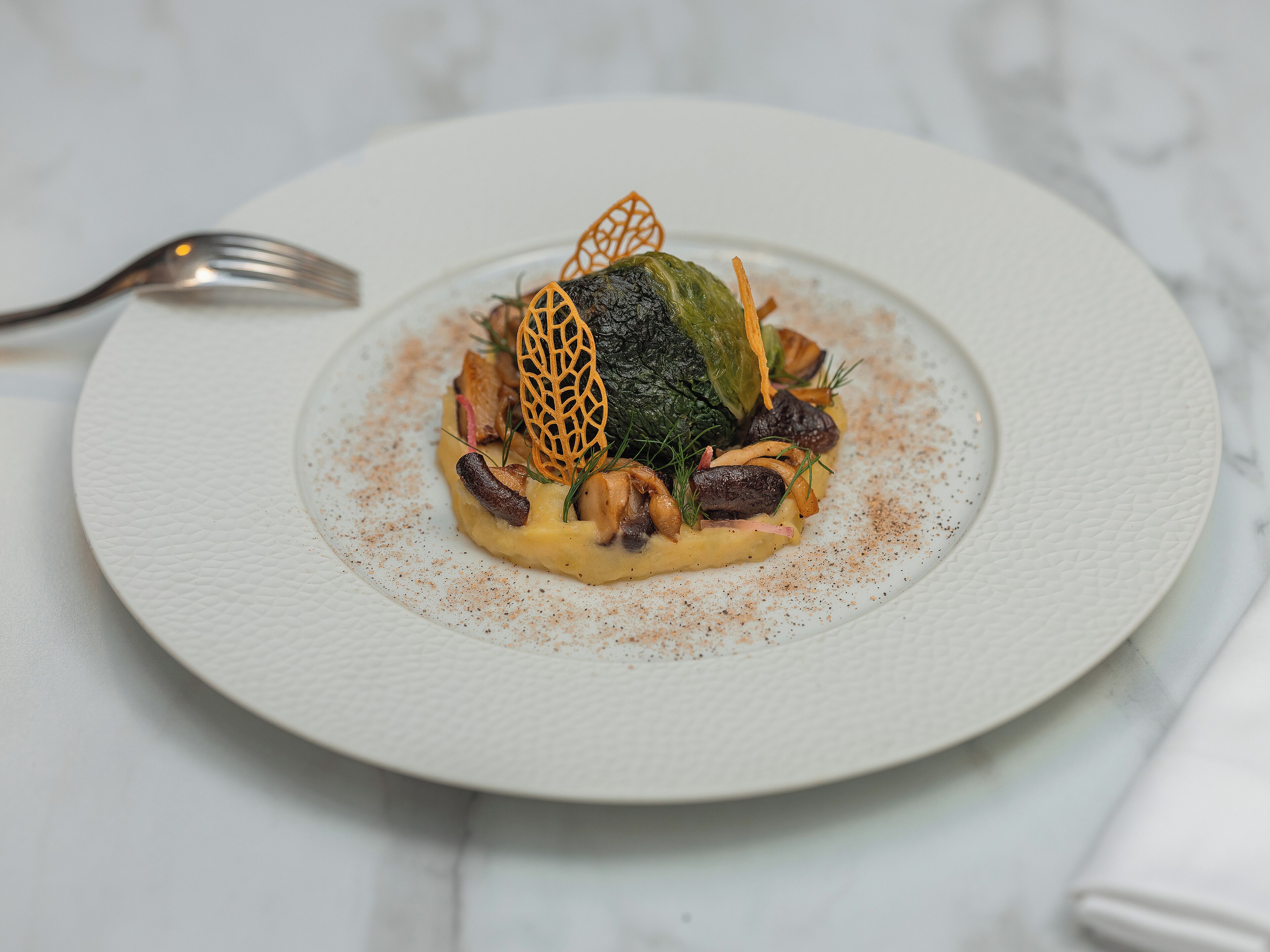 Une assiette blanche contenant un plat, une fourchette et une serviette, le tout posé sur une surface en marbre.