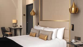 Quarto de hotel com uma cama grande, uma escrivaninha, uma cadeira e duas luzes pendentes.