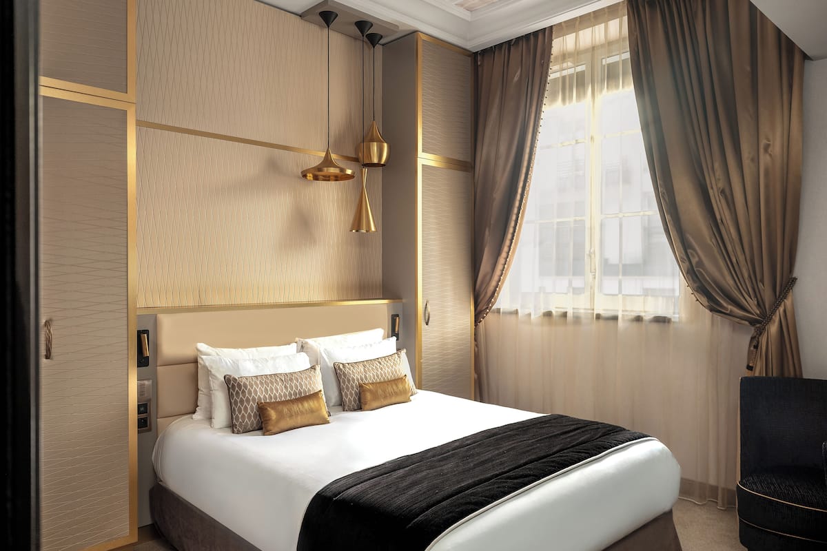A hotel room with a large bed, a nightstand, a chair, and a window with curtains.