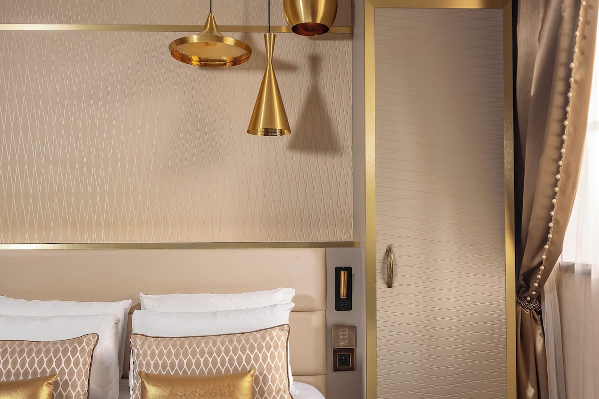 A hotel room with a large bed, two gold-toned lamps, a control panel, and a sliding door.
