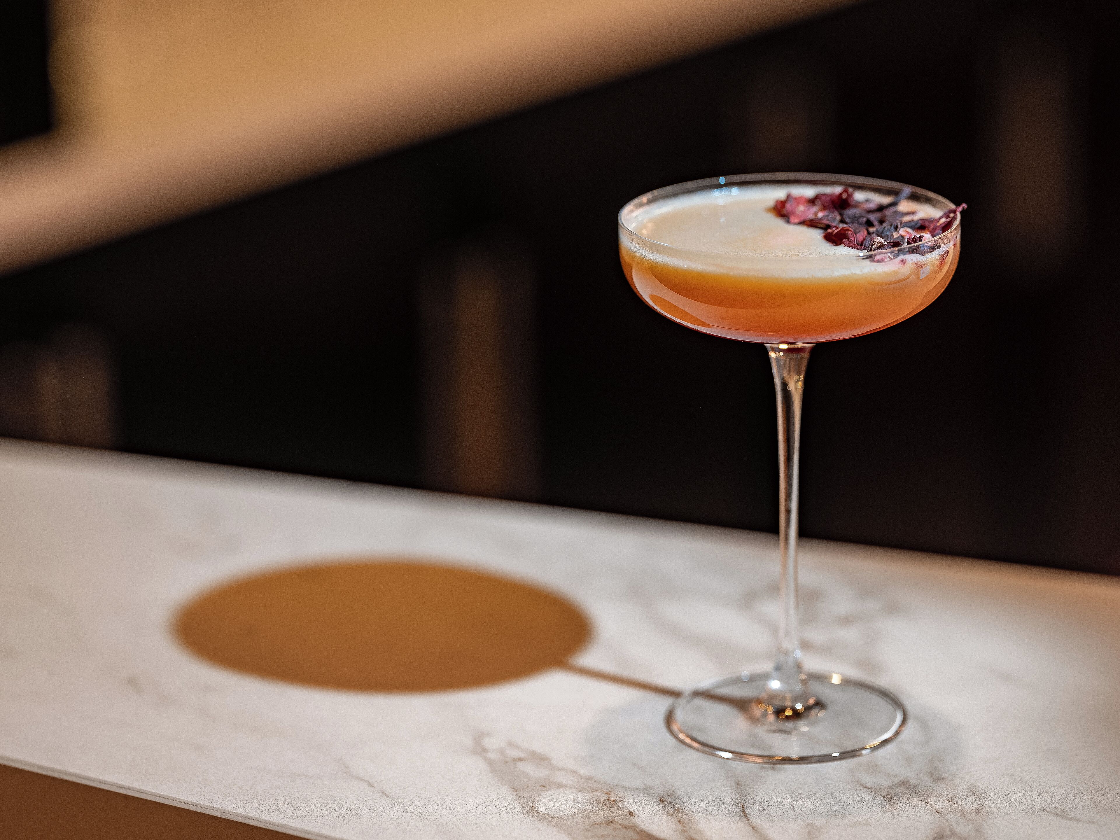 Un verre à martini contenant une boisson à plusieurs couches, posé sur une surface en marbre.