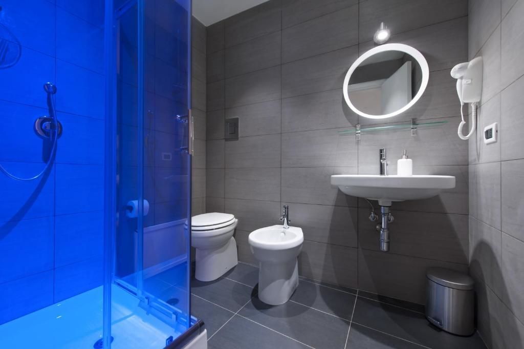 Une salle de bain moderne dotée d’une douche à parois de verre, de toilettes, d’un bidet, d’un lavabo avec un miroir et d’un téléphone.