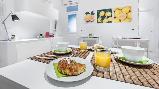 A breakfast setup with croissant, orange juice, and coffee in a bright, modern room with white furniture and a window. - Zero room & breakfast (Palermo)