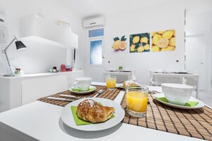 Colazione con croissant, succo d'arancia e caffè in una stanza luminosa e moderna, arredata in bianco e con una finestra.