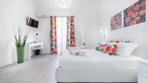 A modern bedroom with a white bed, colorful floral curtains, a desk with a chair, and a TV mounted on the wall. - Zero room & breakfast (Palermo)