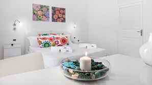 A modern bedroom with a bed, bedside tables, a nightstand, a wall-mounted lamp, and a decorative candle on a glass table. - Zero room & breakfast (Palermo)