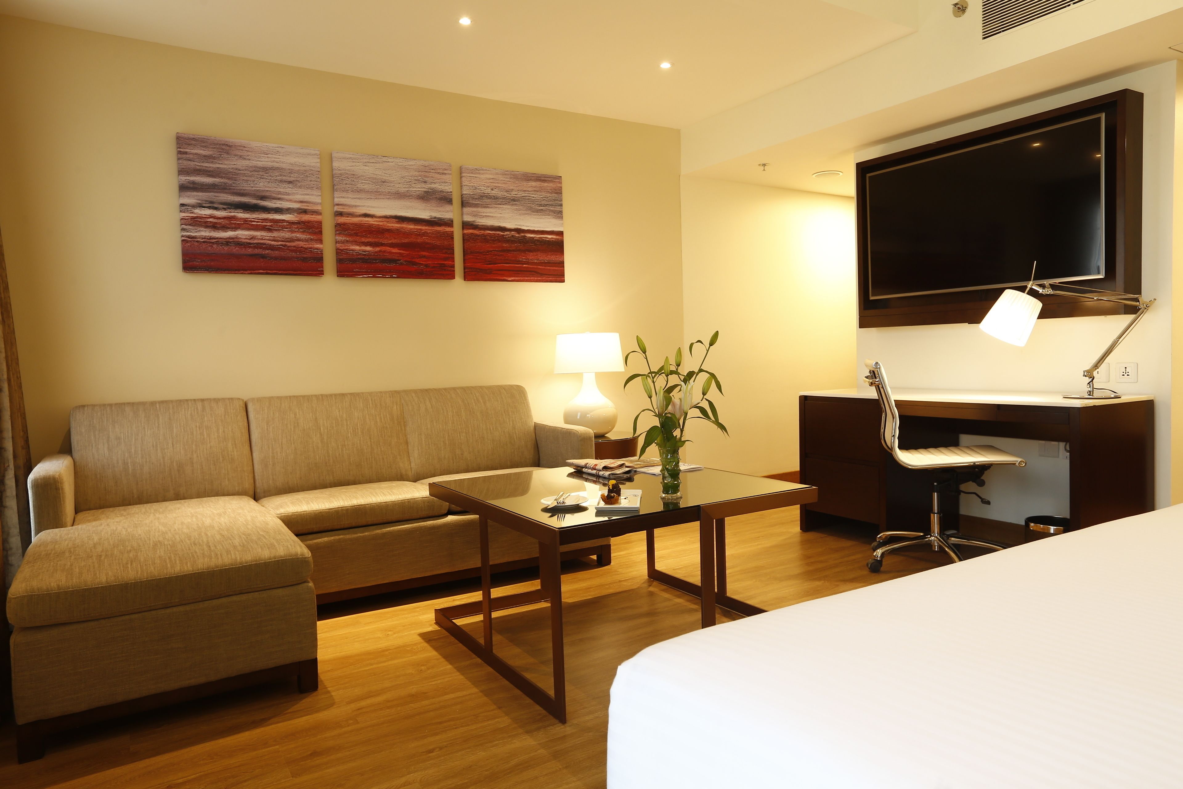 A hotel room with a sofa, a coffee table, a desk with a chair, a TV, and artwork on the wall.