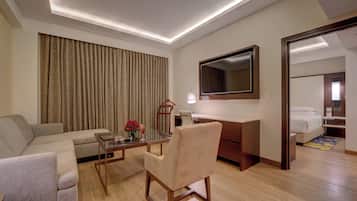 A modern hotel room with a sofa, a glass table, a chair, a desk, a mirror, and a bed.