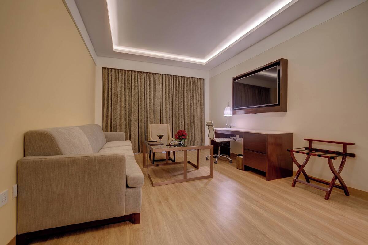 A modern hotel room with a sofa, desk, and mirror.