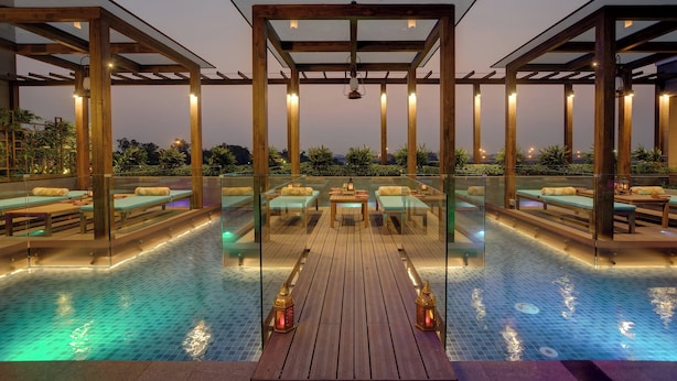 A rooftop pool area with wooden deck, glass railings, and seating arrangements. - Courtyard by Marriott Surat (Surat)