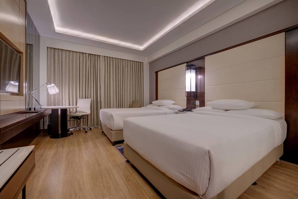 A hotel room with two beds, a desk, a chair, and a large mirror.