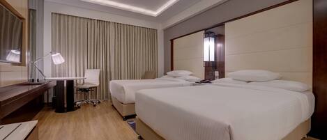 A hotel room with two beds, a desk, a chair, and a large mirror.
